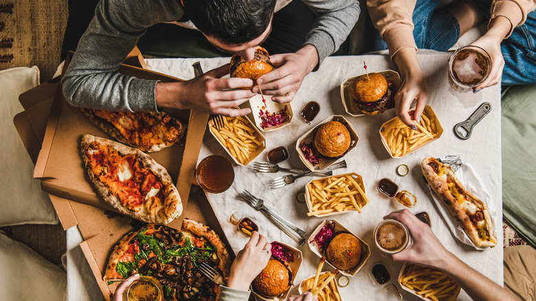 people seated at a table eating junk food hamburger pizza fries