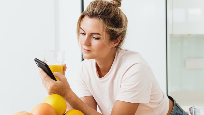Woman looking at phone holding juice