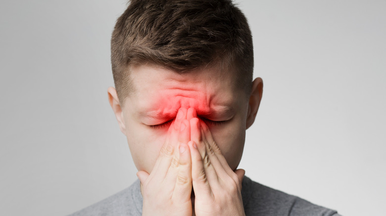 Man suffering from sinus pressure, touching his nose with closed eyes