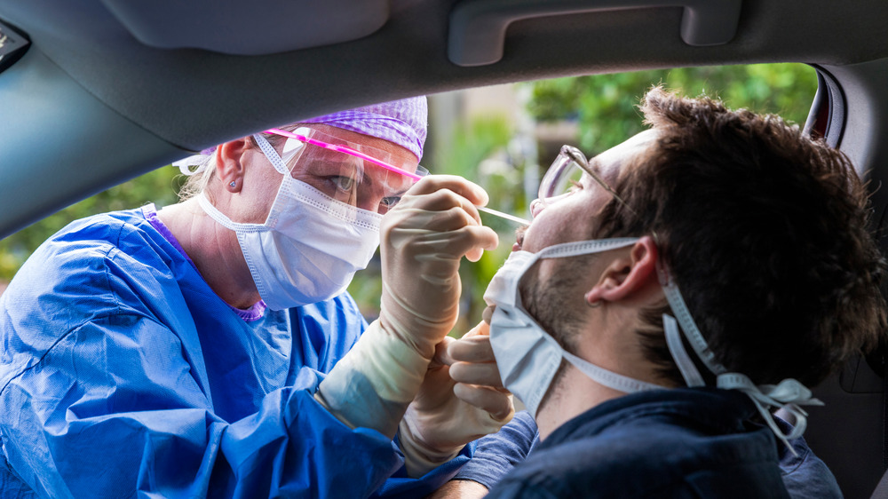 Health care worker performing nasal swab test on patient in car