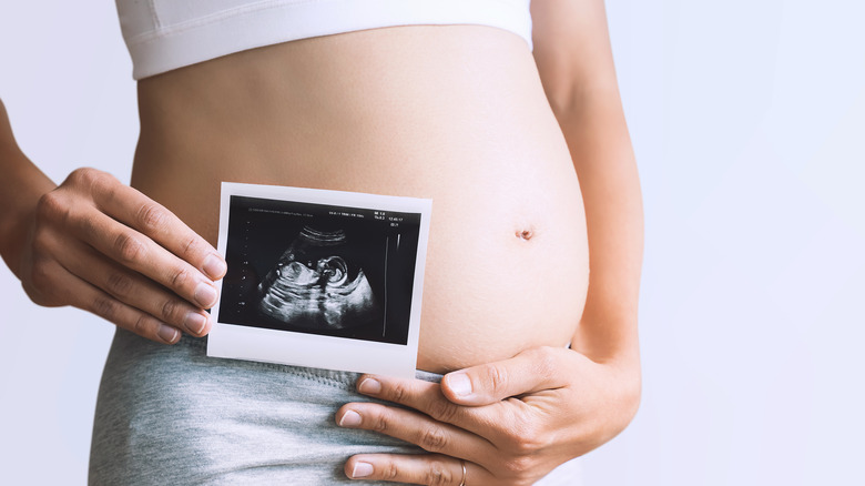 Pregnant woman holding ultrasound photo up close by stomach