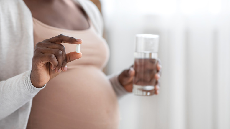 Closeup of a pregnant woman holding a white pill and glass of water