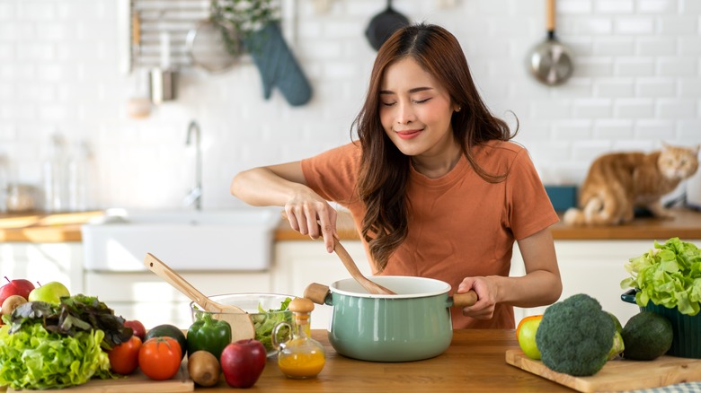 woman stirring a pot next to vegetables