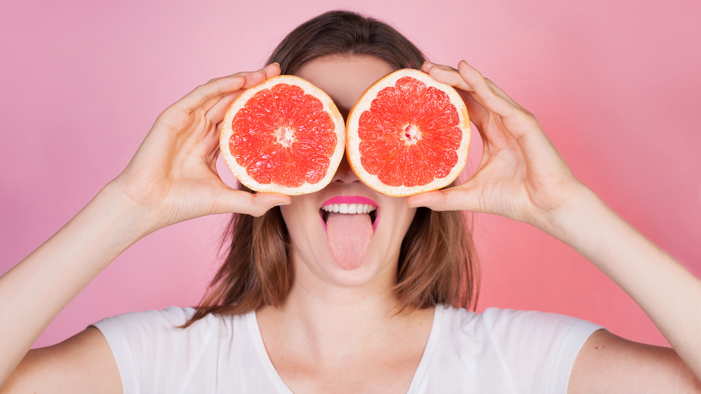 woman holding sliced grapefruit over eyes