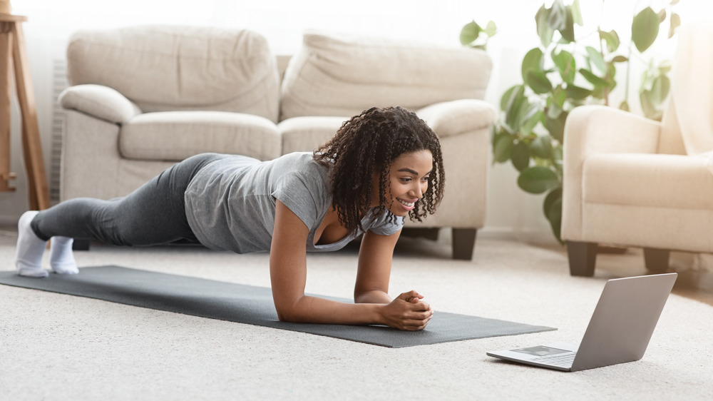 Fit black woman doing yoga plank while watching online tutorial on laptop