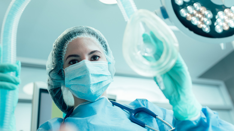 A medical professional dressed for surgery holding an anesthesia mask 