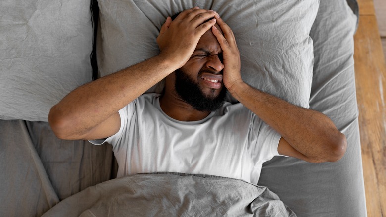 Man laying in bed holding his head and making stressed facial expression