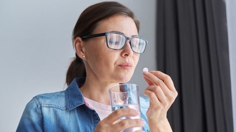 Woman with glasses taking a pill with a glass of water