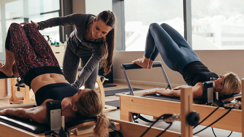 Instructor guiding students on a Pilates reformer
