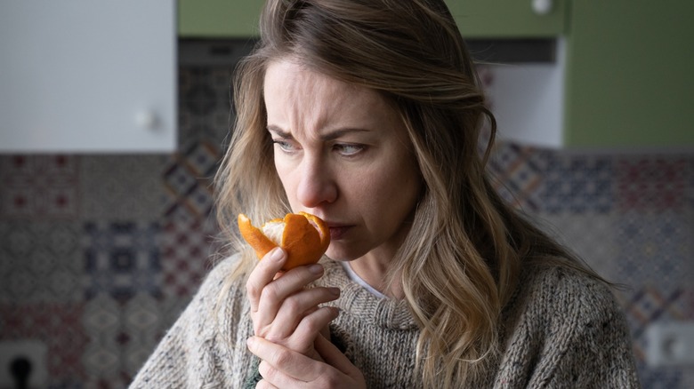 woman wrinkling brow while sniffing orange