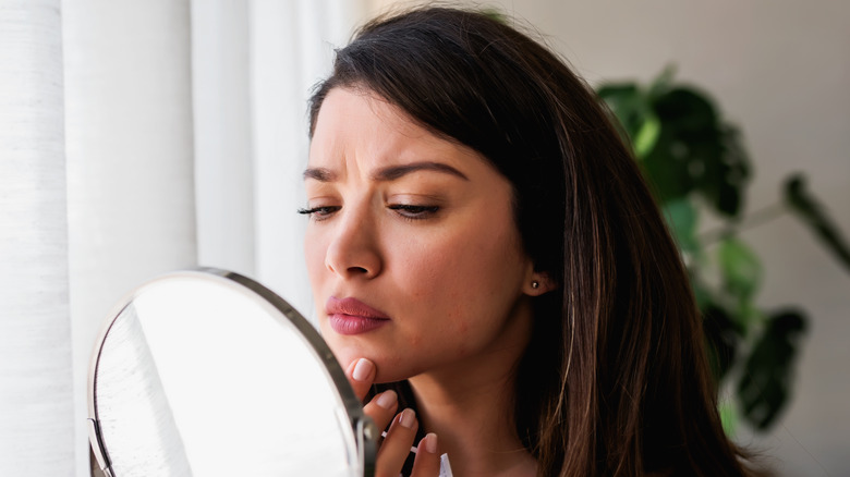 woman examining acne in a mirror