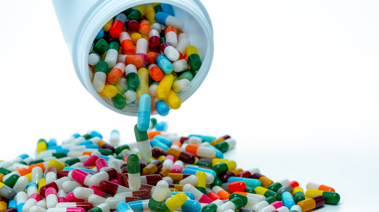 Multi-colored antibiotic capsules pour out of a white pill bottle into a pile
