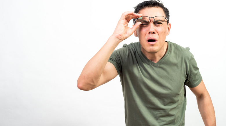 Man squinting while lifting glasses off his nose and having trouble seeing clearly