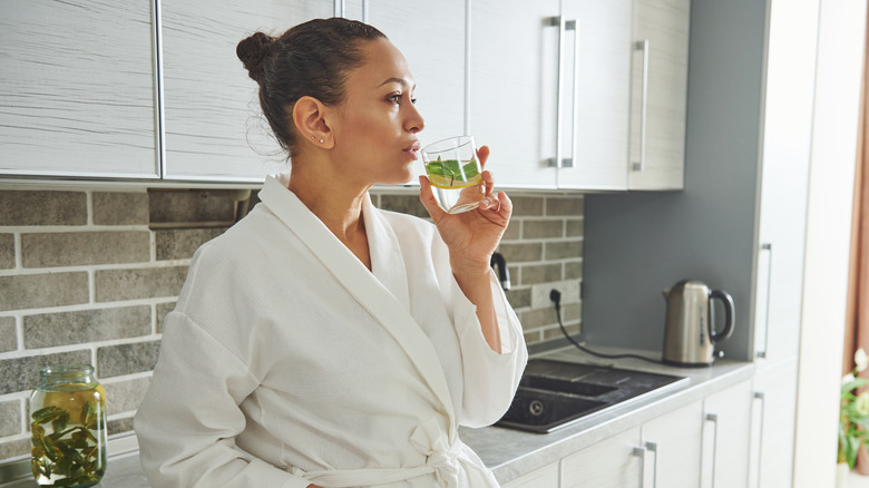 woman in white robe drinking a glass of water