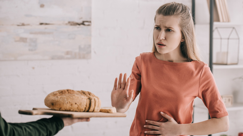 woman holding her belly while pushing away bread