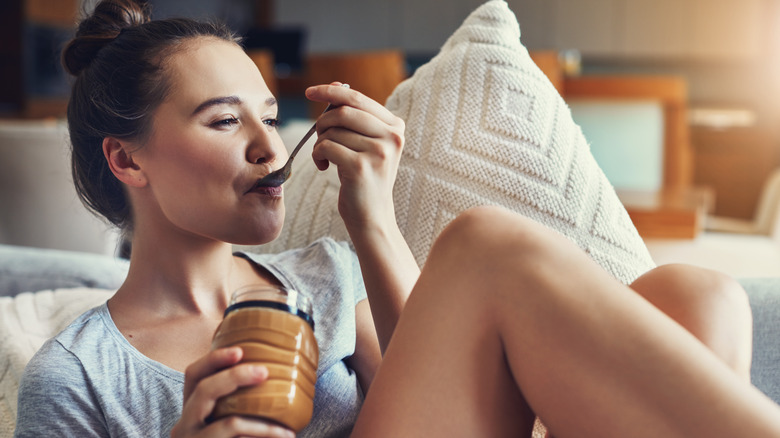 Woman smiling while eating peanut butter from jar