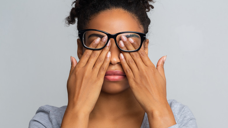 A woman with glasses rubs her eyes