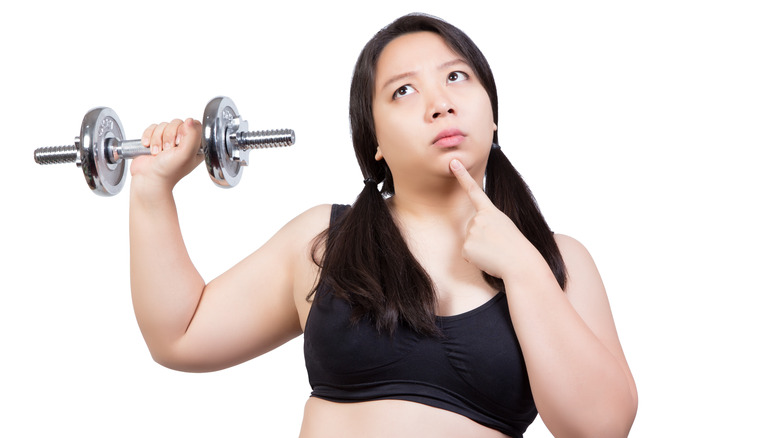 confused-looking woman holds dumbbell