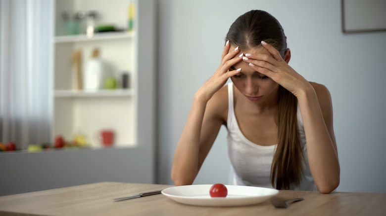 Girl stares at a plate with one tomato on it hungry