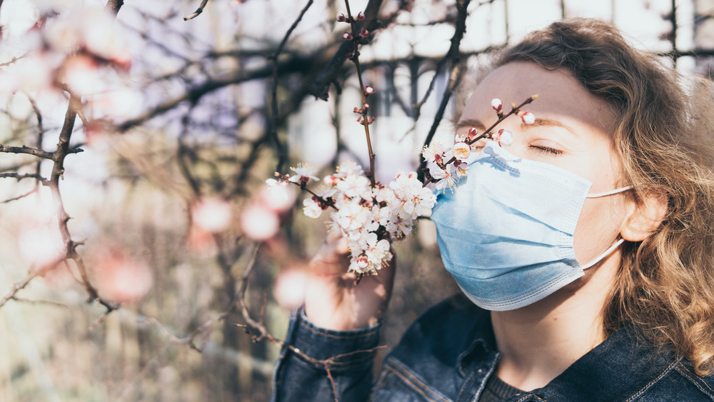 Woman wearing a face mask sniffs tree blossoms