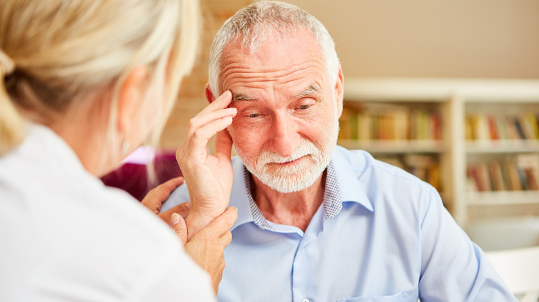 A caretaker talking to an elderly man while he touches his head