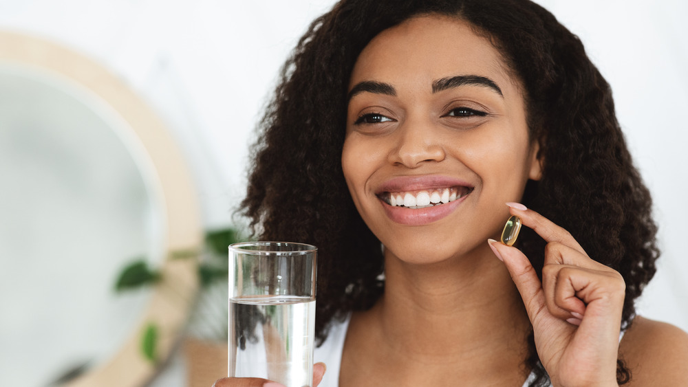 Woman holding glass of water and fish oil supplement