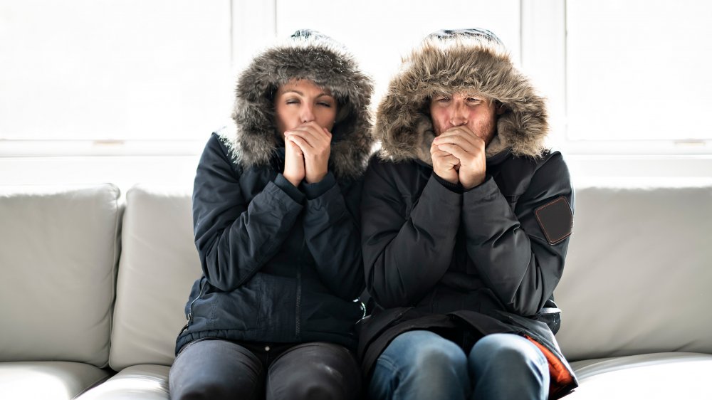 Couple bundled in winter coats on sofa and coughing