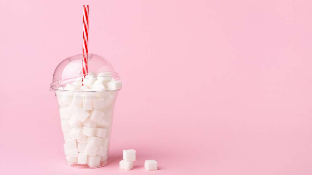 A plastic cup filled with sugar cubes with a pink background 