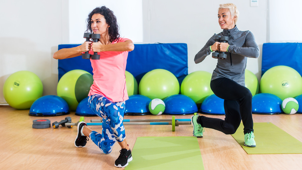 Two women holding hand weights and performing curtsy lunges