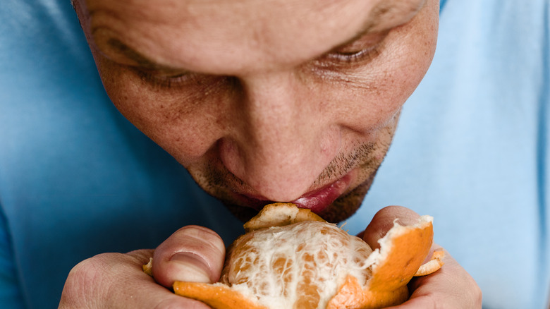 man in blue shirt trying to smell an orange