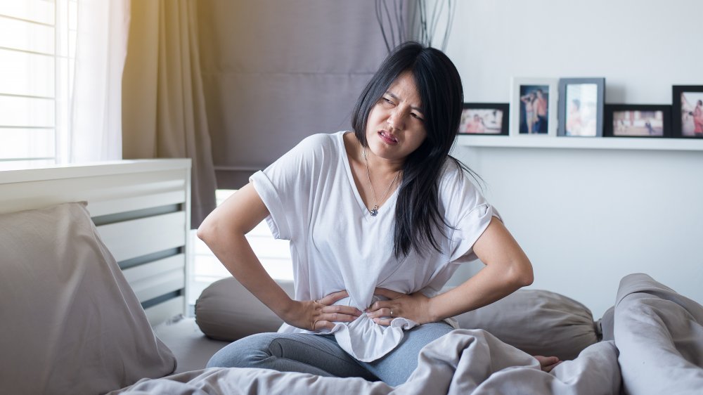 Woman sitting on bed holding abdomen