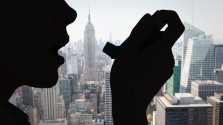 Silhouette of person using inhaler against a city skyline
