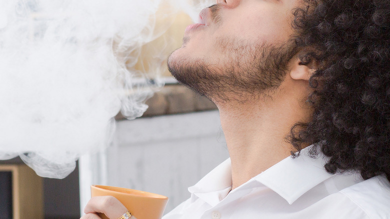 Man blowing smoke and drinking coffee