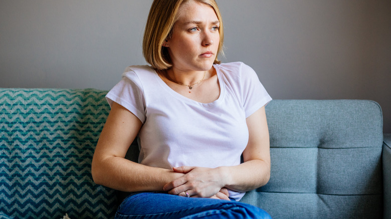 woman holding her stomach while sitting on the couch