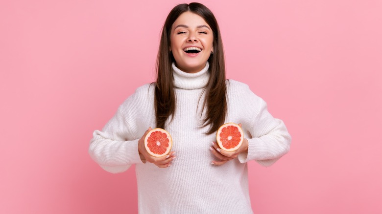 woman holding grapefruit at breasts
