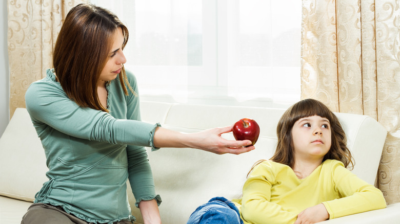 A mom tries to get her daughter to eat an apple