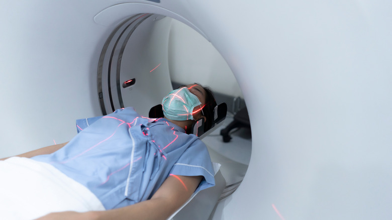 Person lies in CT scanning machine with red laser lines on her body that help technicians line her body up correctly for imaging