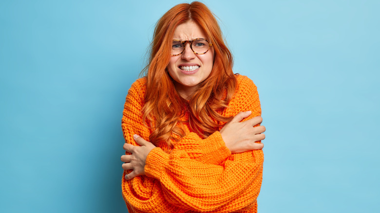 Woman wearing glasses and orange sweater holding her arms feeling cold