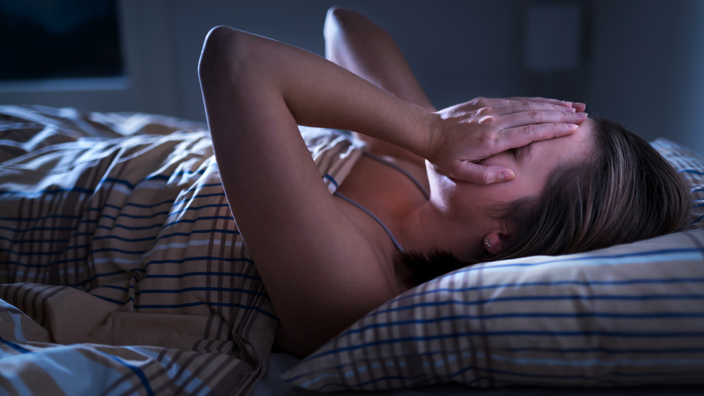 Woman laying in bed at night with her hands over her eyes