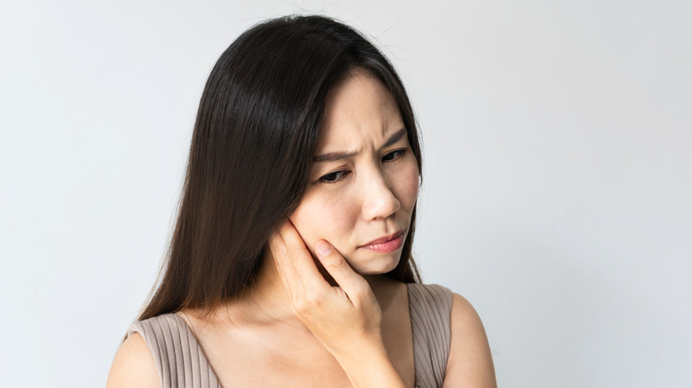A woman cradles her jaw to indicate oral discomfort