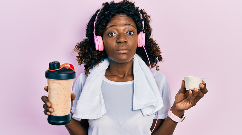 Surprised woman holding protein shake and powder