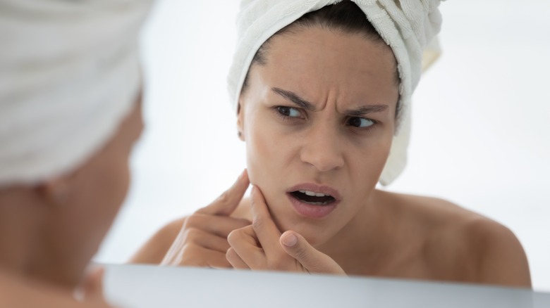 Upset woman looking at skin in mirror