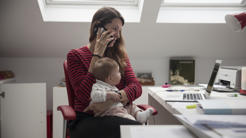 Woman in front of a laptop on a phone with a baby on her lap