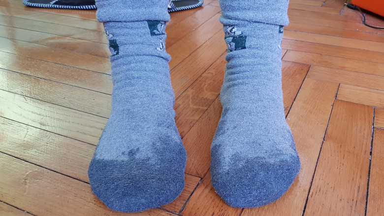 Pair of feet standing in wet pair of blue socks on wooden floor
