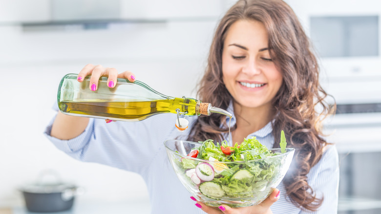 woman pouring olive oil on salad